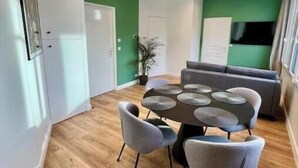 A modern dining area with a round table and grey chairs, a sofa, and a green accent wall. - Very bright, recently renovated apartment with air conditioning (Île-de-France)