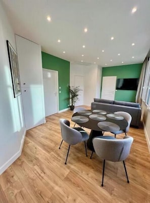 Ein moderner Essbereich mit einem runden Tisch, grauen Stühlen, einer Couch und einer Wand in Grünton.