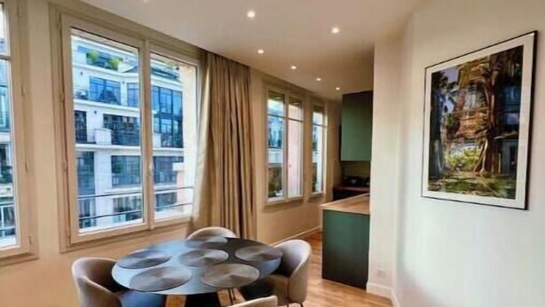 A dining area with a round table and chairs, large windows, and a painting on the wall. - Very bright, recently renovated apartment with air conditioning (Île-de-France)
