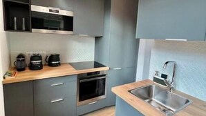 A modern kitchen with grey cabinets, a wooden countertop, and stainless steel appliances. - Very bright, recently renovated apartment with air conditioning (Île-de-France)