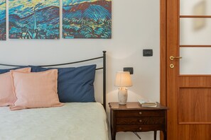 A bedroom with a bed, pillows, a bedside table with a lamp, a book, and two paintings on the wall. - Finestra sulle Porte Palatine by Wonderful Italy (Turin)