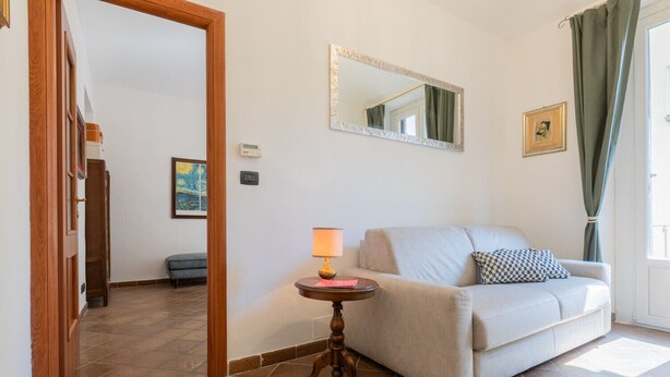 Uma sala de estar com um sofá, uma luminária, um espelho e uma porta que dá para outro cômodo.