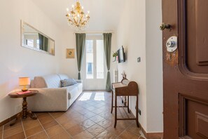 Ein Zimmer mit einer Couch, einer Lampe, einem Tisch, einem Stuhl, einem Spiegel, einer Deckenleuchte und einer Tür.