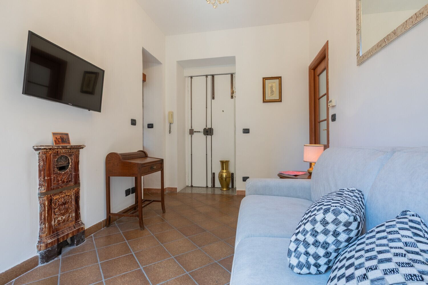 Un salon comprenant un canapé, un téléviseur fixé au mur, un meuble en bois et une porte donnant sur une autre pièce.