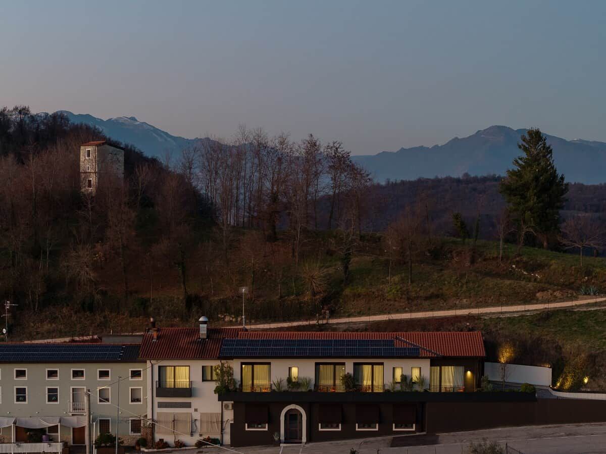 A building with multiple windows and a red roof, surrounded by trees and mountains in the background.