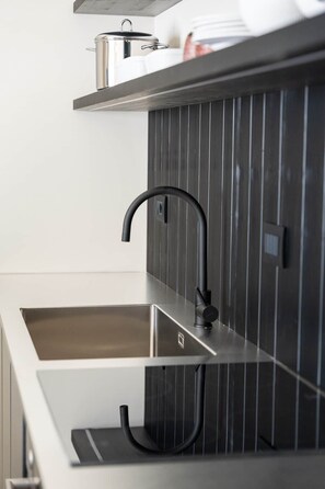 Cocina moderna con pileta de acero inoxidable, grifo negro y panel de madera en la pared.
