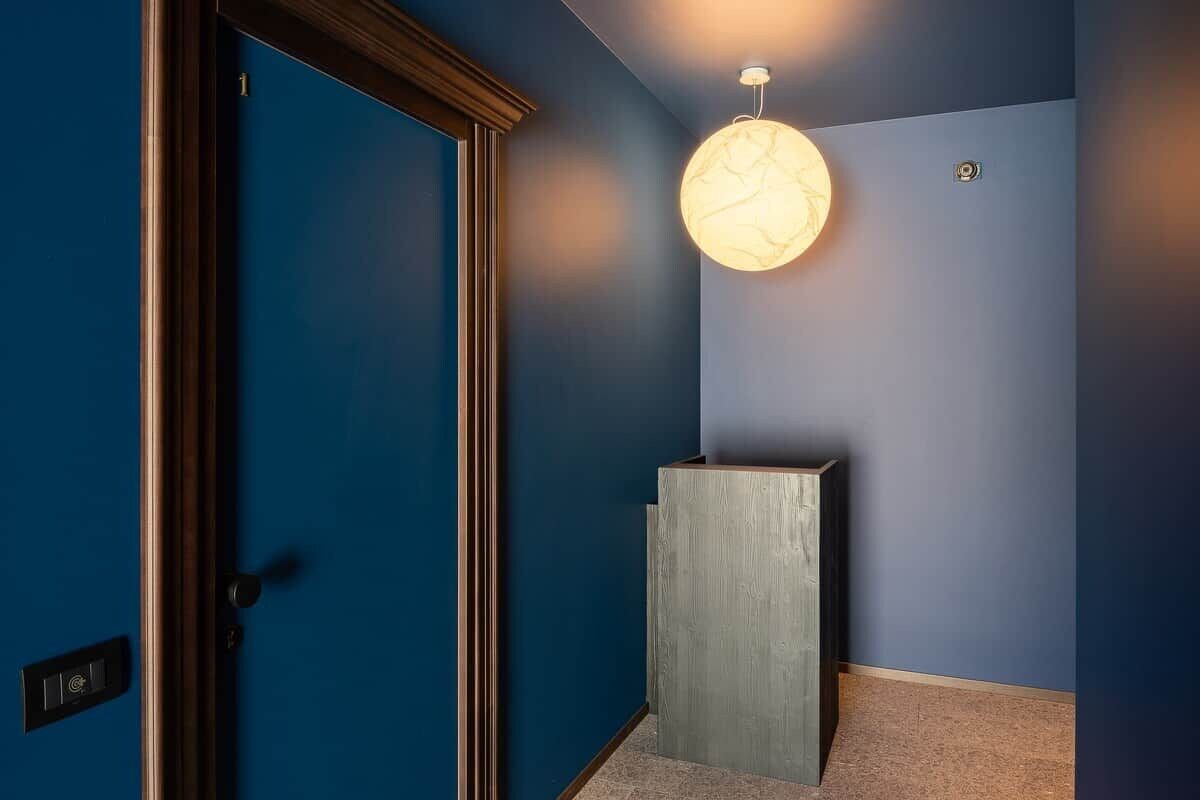 A hallway with a blue wall, a wooden door, and a light fixture.