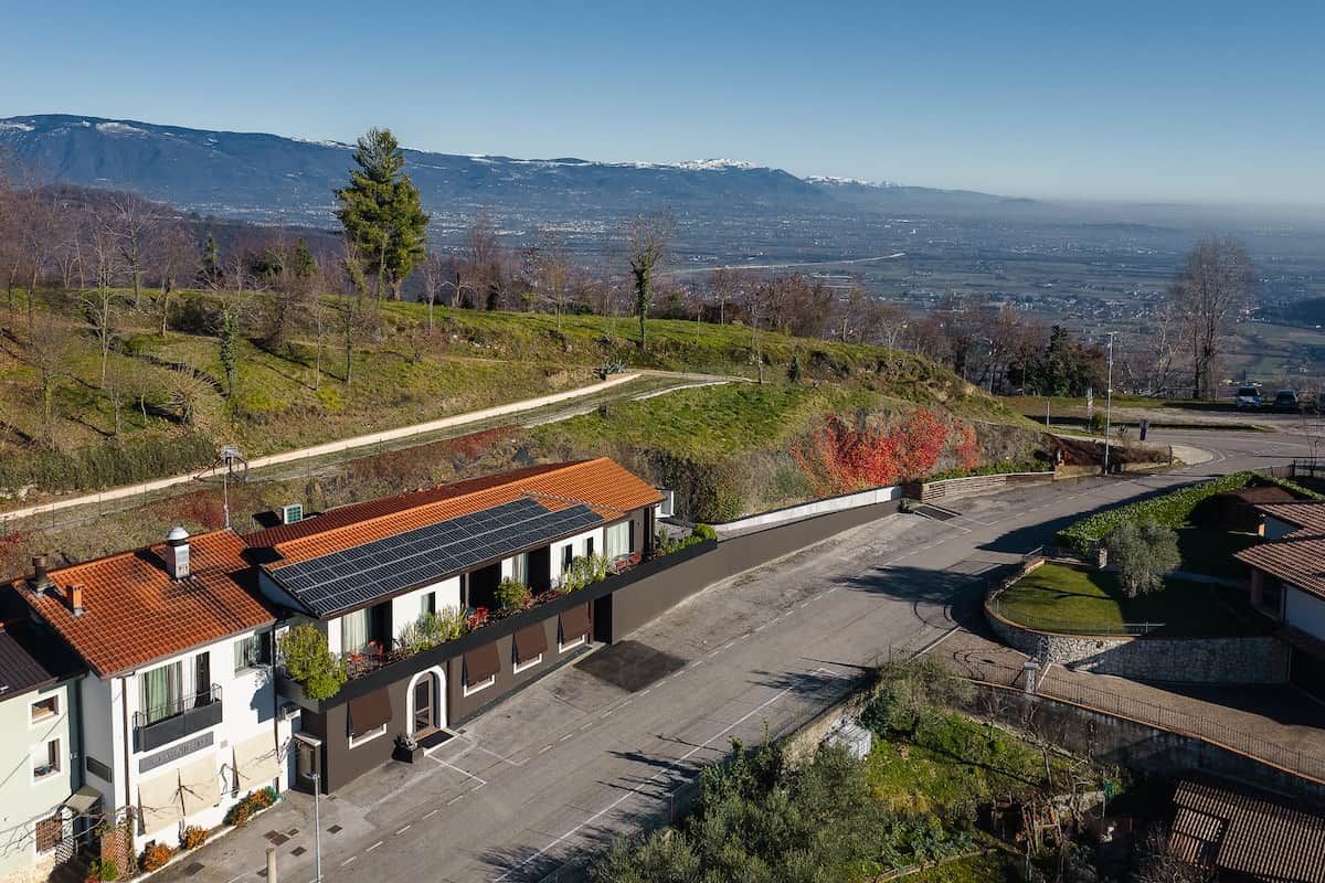 A residential area with a house featuring a solar panel roof, a paved driveway, and a view of distant mountains.