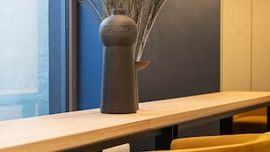 En modern inredning med ett långt bord, gula stolar och en vas med torkade växter.