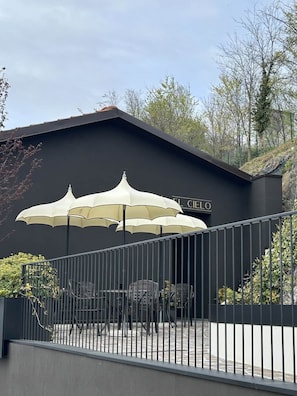 Un bâtiment à la façade noire, sur lequel on peut lire l’inscription « EL CIELO ». On y voit trois parasols blancs qui font de l’ombre, ainsi qu’une clôture métallique au premier plan.