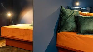 Ett modernt rum med en soffa och en säng, båda med orange sängkläder. Rummet har ett trägolv och en blå accentvägg.