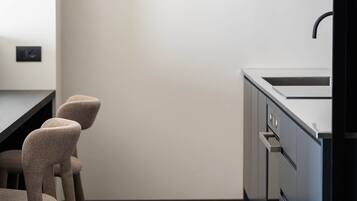 Cocina moderna con encimera oscura, un lavamanos y una estufa. Hay tres sillas de diseño único.