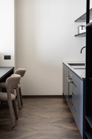 A modern kitchen with a dark countertop, a sink, and a stove. There are three chairs with a unique design.