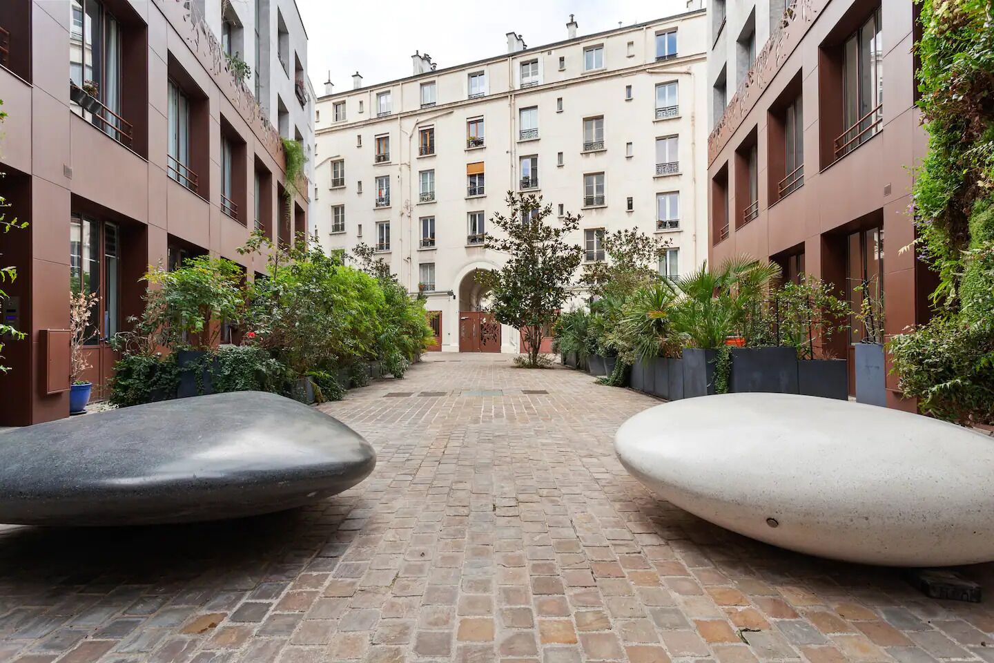 A courtyard with a brick pathway, two large planters, and a building with multiple windows and balconies.