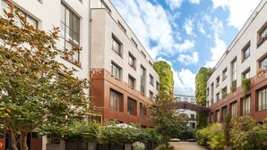 Un patio con sendero de ladrillo, rodeado de edificios con amplias ventanas y un árbol.