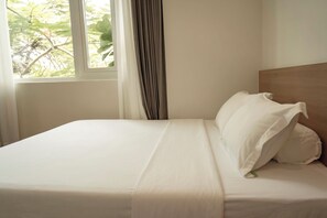 A neatly made bed with white linens in a room with a window and curtains. - Heyday Premium by Nomah (Ho Chi Minh City)