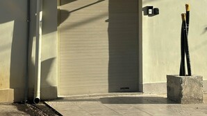 Loja fechada com toldo listrado, uma câmera de segurança e um bloco de concreto na calçada.