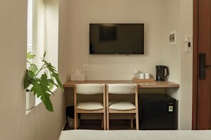 A compact hotel room with a bed, a desk with two chairs, a television, a small refrigerator, and a potted plant. - Heyday Premium by Nomah (Ho Chi Minh City)