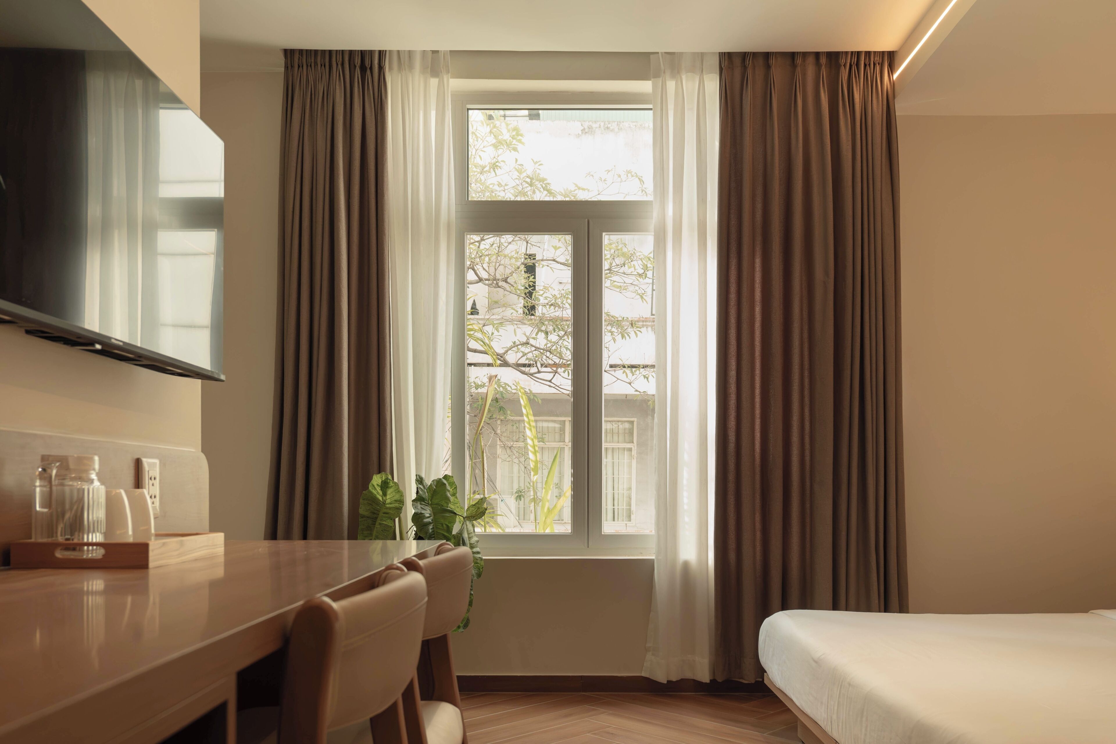 Une chambre d’hôtel comprenant un lit, un bureau avec des chaises, une télévision et une fenêtre avec des rideaux.