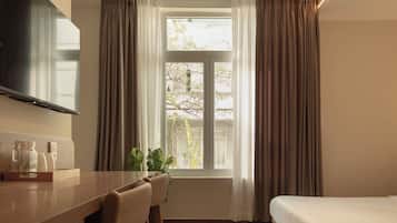Une chambre d’hôtel comprenant un lit, un bureau avec des chaises, une télévision et une fenêtre avec des rideaux.