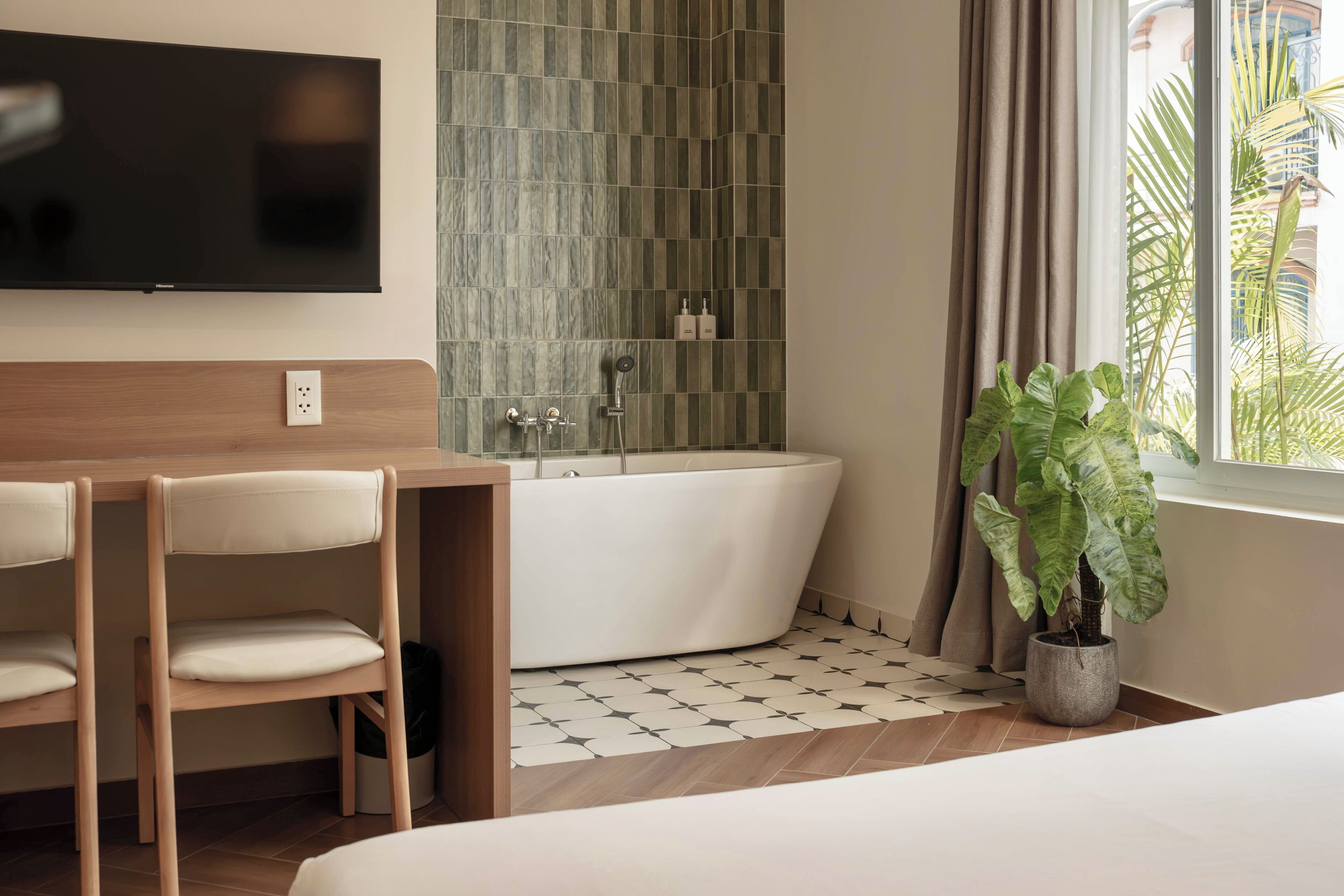 Een moderne badkamer met een vrijstaand bad, een televisie aan de muur en een plant in een pot bij het raam.
