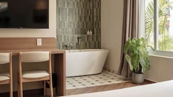 Een moderne badkamer met een vrijstaand bad, een televisie aan de muur en een plant in een pot bij het raam.