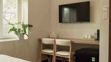 Ein Hotelzimmer mit einem Bett, einem Schreibtisch mit zwei Stühlen, einem Fernseher und einer Zimmerpflanze.