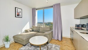 A modern living room with a sofa, a round coffee table, and a view of the outdoors. - One Rosebank Apartment- Studio (Johannesburg)