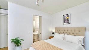 A bedroom with a bed, a potted plant, a framed picture on the wall, and a door leading to a bathroom. - One Rosebank Apartment- Studio (Johannesburg)