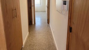 Un corridoio con porte in legno, pavimento piastrellato e vista su una stanza con finestra e tende.