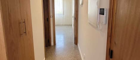 A hallway with wooden doors, a tiled floor, and a view into a room with a window and curtains.