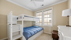 Quarto com beliches, janela com persianas, ventilador de teto e mesa de cabeceira com abajur.