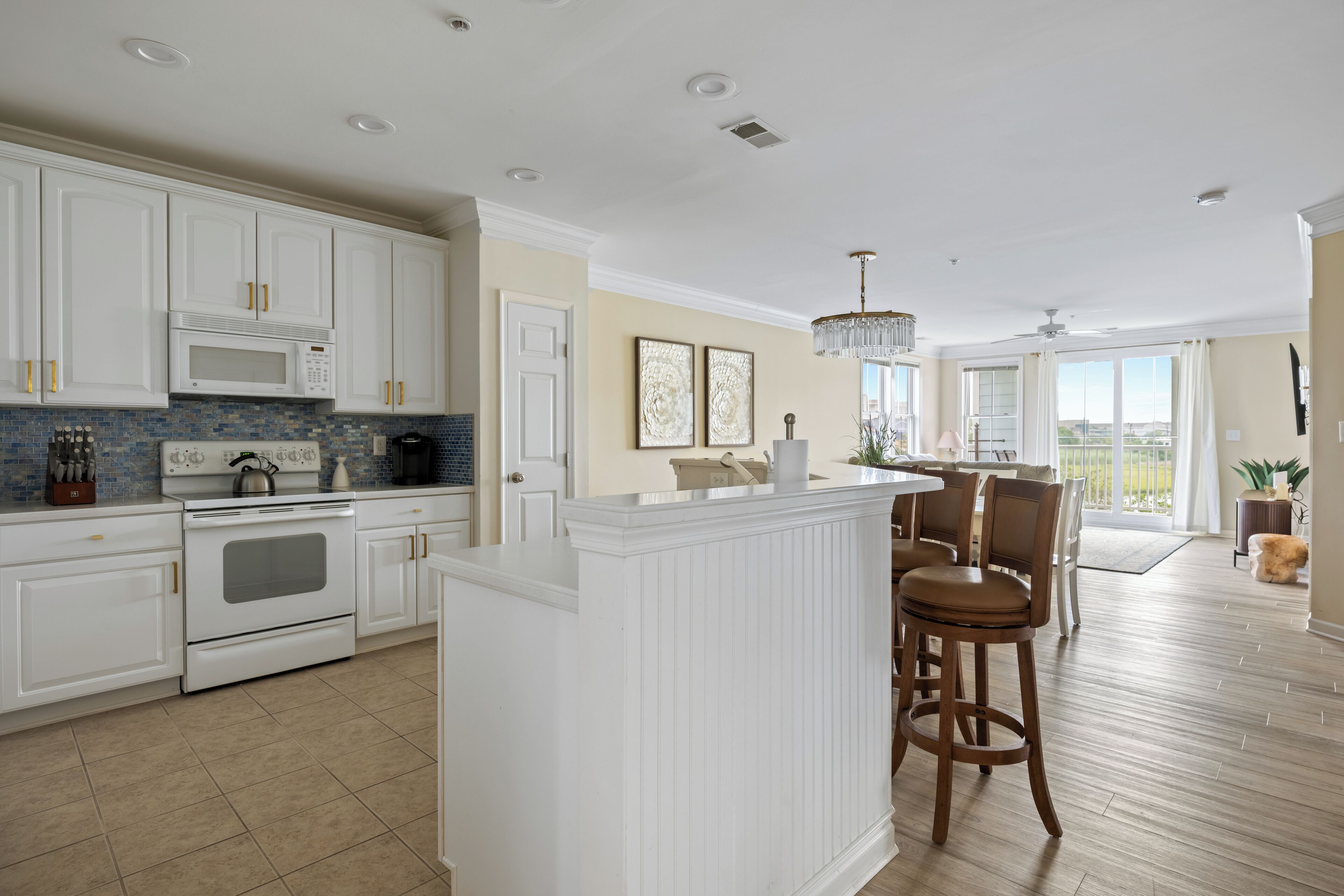 A modern kitchen with white cabinetry, a central island, and a dining area with wooden chairs.