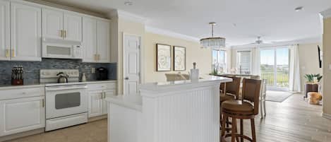 Une cuisine moderne avec des meubles blancs, un îlot central et un coin repas doté de chaises en bois.