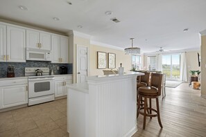 Una cocina moderna con armarios blancos, una isla central y una zona de comedor con sillas de madera.