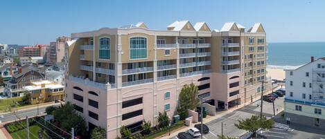A multi-story hotel with balconies, parking, and a view of the beach.