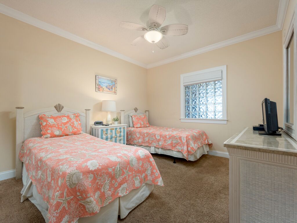 Un dormitorio con dos camas, un ventilador de techo, una ventana con vidrieras decorativas y un aparador.