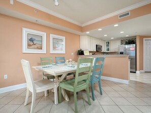 A dining area with a table and chairs, a kitchen in the background, and framed artwork on the wall. - South Beach is a luxurious building overlooking the boardwalk, beach and ocean. (Ocean City)