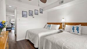 A hotel room with two beds, a wooden dresser, and a desk with a vase of flowers. - Jamaica Day Break N 407 – Bayside Comfort in the Heart of Midtown (Ocean City)
