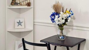 A corner with a white shelving unit, a framed picture, a vase with flowers, and a dark wooden chair. - Jamaica Day Break N 407 – Bayside Comfort in the Heart of Midtown (Ocean City)