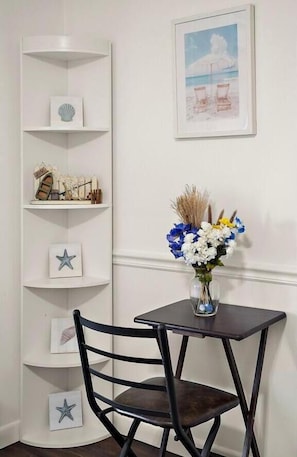 Eine Ecke mit einem weißen Regal, einem gerahmten Bild, einer Blumenvase und einem dunklen Holzstuhl.