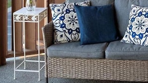 A balcony with wicker furniture, a small table with a vase of flowers, and decorative wall art. - Jamaica Day Break N 407 – Bayside Comfort in the Heart of Midtown (Ocean City)