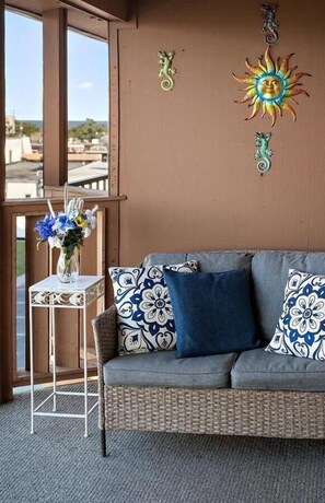Ein Balkon mit Korbmöbeln, einem kleinen Tisch mit Blumen und dekorativer Wandkunst.