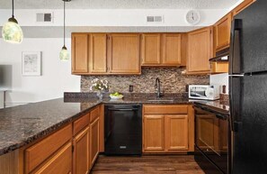 Eine Küche mit Holzausstattung, einer Arbeitsplatte aus Granit, einem schwarzen Geschirrspüler und einem Kühlschrank.