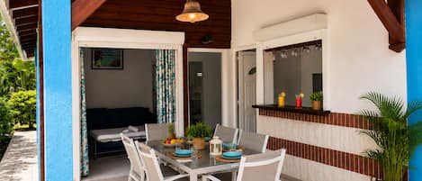 Un patio techado al aire libre con una mesa de comedor, sillas y una lámpara colgante.