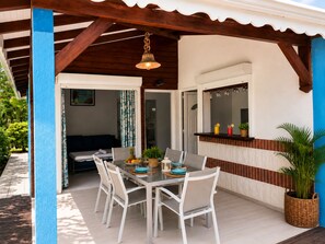 Eine überdachte Terrasse mit Esstisch, Stühlen und einer hängenden Leuchte.