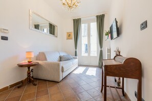 A hotel room with a sofa, a small table with a lamp, a wooden desk, a television, and a window with curtains. - Finestra Sulle Porte Palatine by Wonderful Italy (Turin)