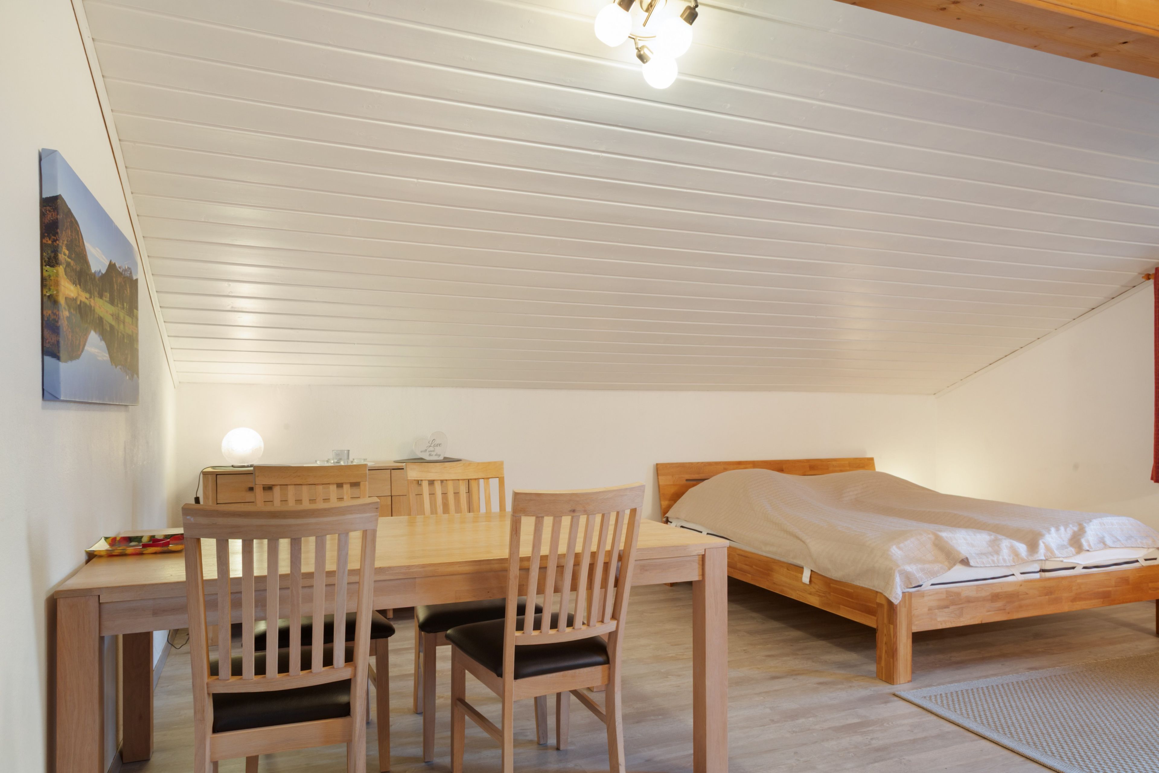 A bedroom with a wooden bed, a desk with a chair, and a ceiling light fixture.