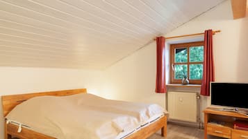 Une chambre à coucher avec un lit en bois, une fenêtre avec des rideaux, un radiateur et un téléviseur posé sur un meuble en bois.