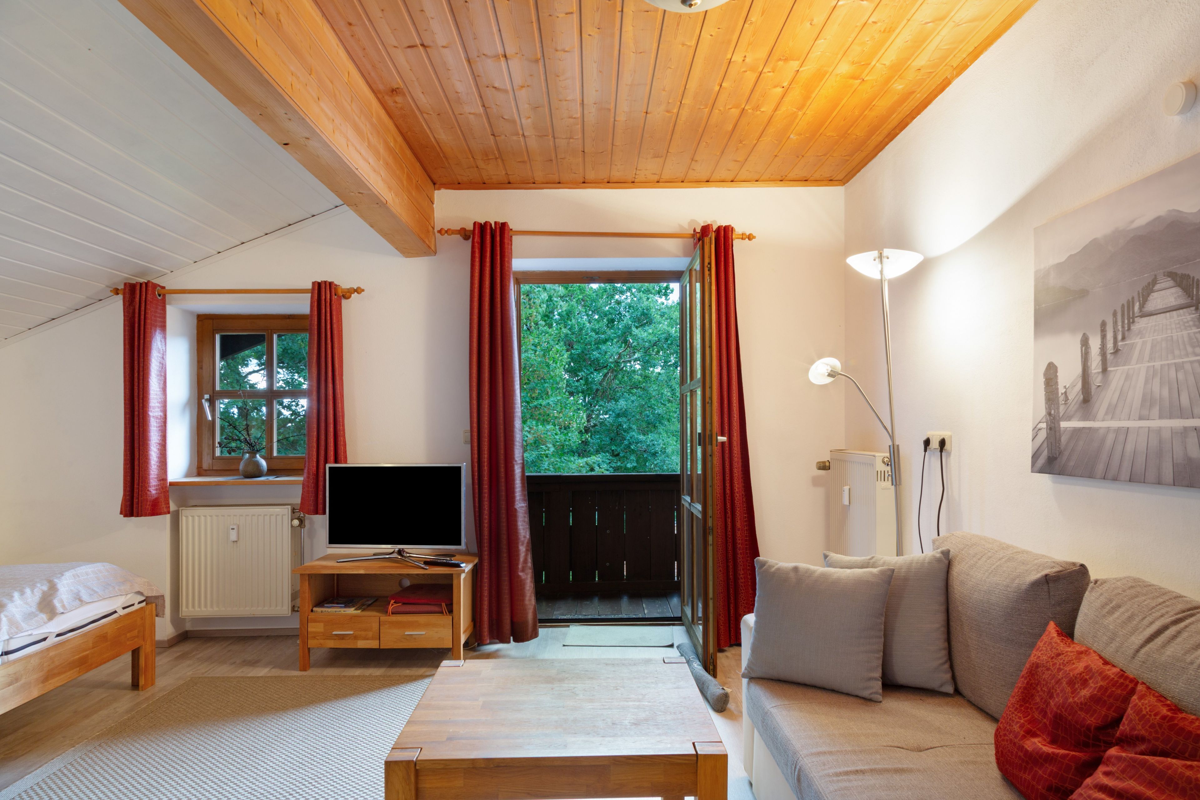 Une pièce confortable avec un plafond en bois, un lit, une télévision, un canapé et une fenêtre avec des rideaux.